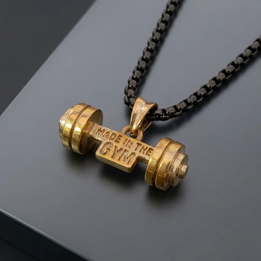 Gold dumbbell-shaped pendant on a chain with 'Made in the Gym' text on a dark background