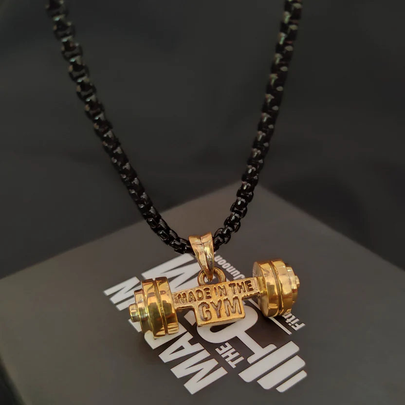 Gold dumbbell pendant necklace hanging on a black chain with 'Made in the Gym' text on a dark background.