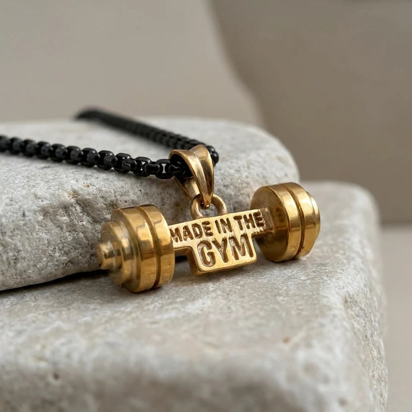 Gold dumbbell-shaped pendant with 'Made in the Gym' text on a stone surface