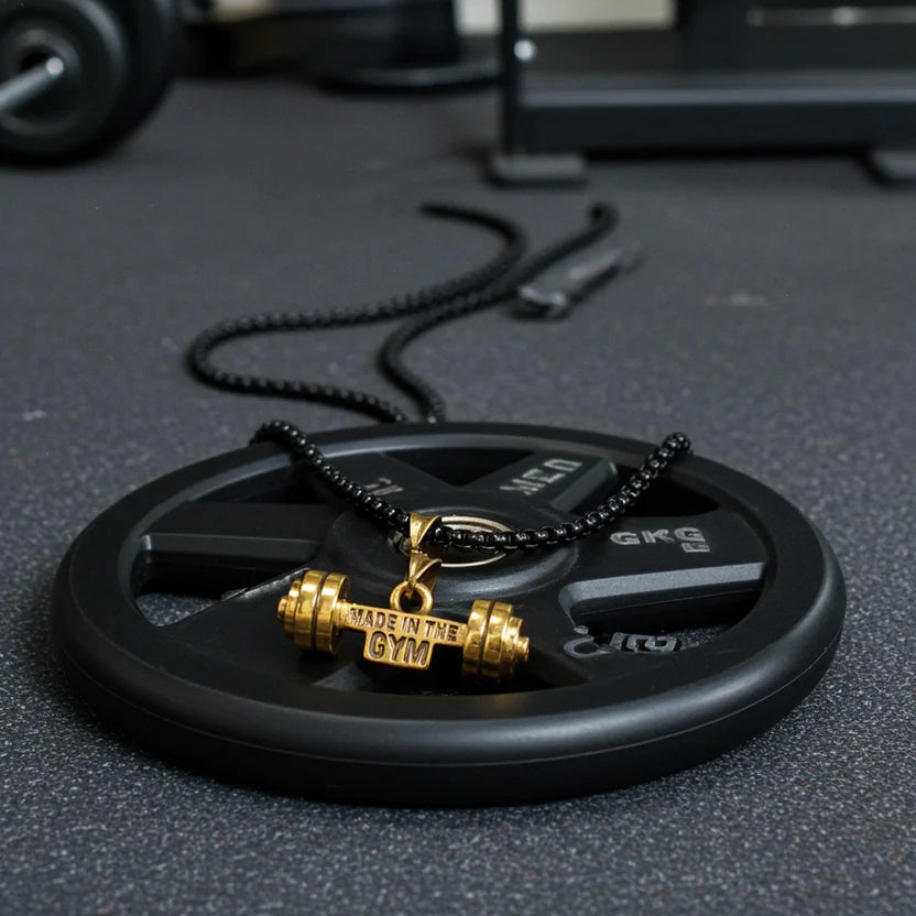 Gold barbell pendant on a black weight plate with gym equipment in the background